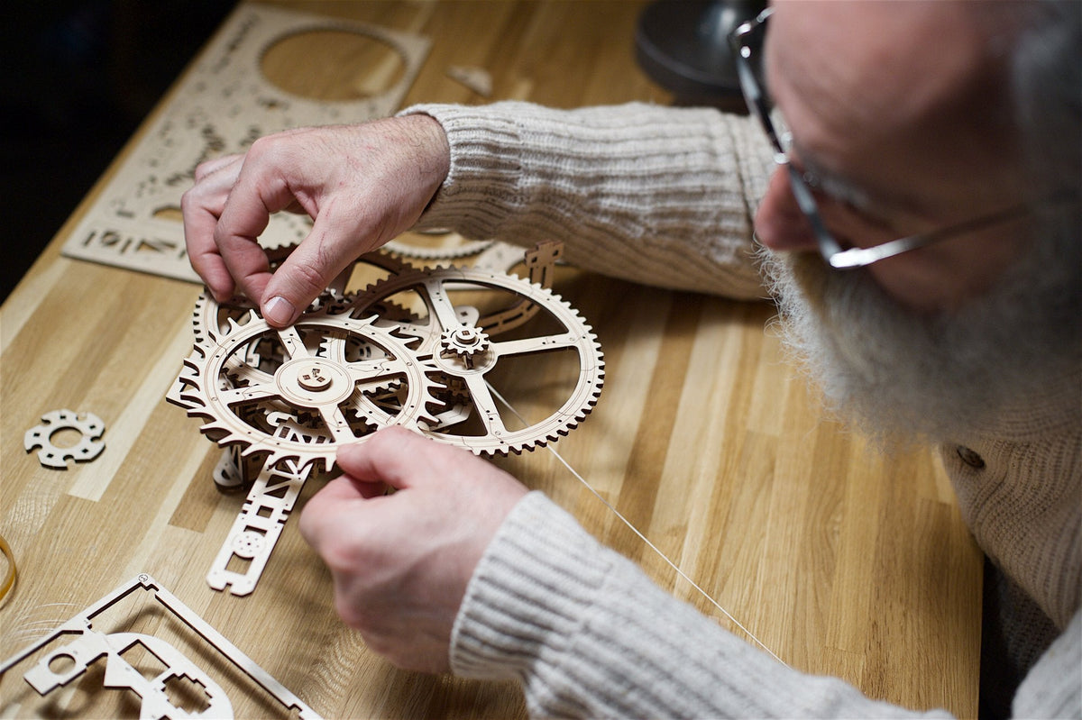 Hands assembling a clock movement of wooden gears