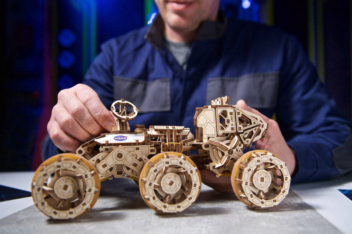 Mann in Arbeitsjacke baut einen Rover aus Holz mit sechs Rädern
