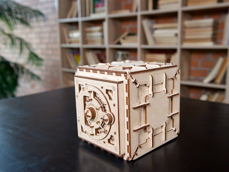 Holzmodell eines Safes auf einem dunklen Tisch vor einem Bücherregal