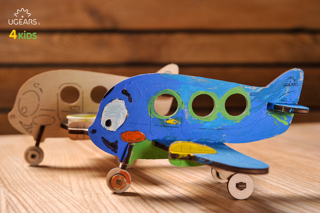 Flugzeug aus Holz, blau bemalt, neben unbemalter Version
